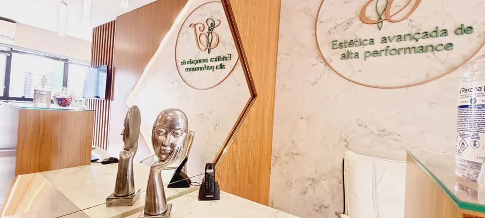 Recepção da Clínica Dra. Jociene com balcão de mármore e painel de madeira, ambiente sofisticado para tratamentos de alta performance